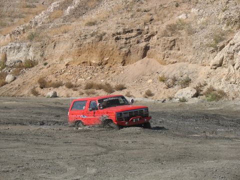 1987 Ford Bronco - A red SUV is stuck in a muddy area with a rocky hillside in the background.