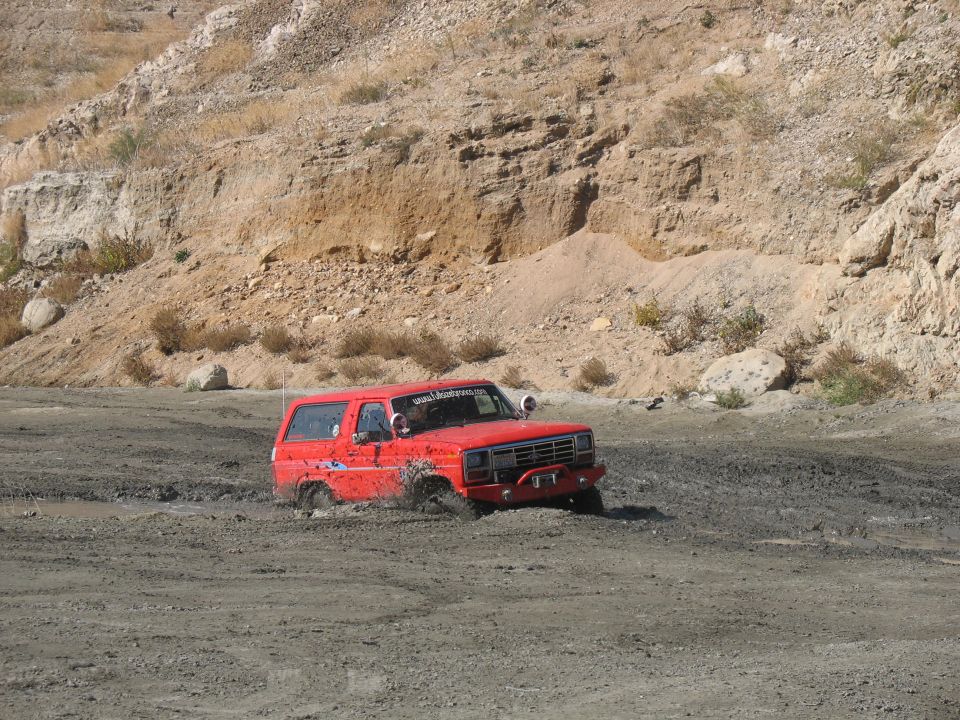 Red SUV stuck in mud, front bumper visible. Website address on windshield