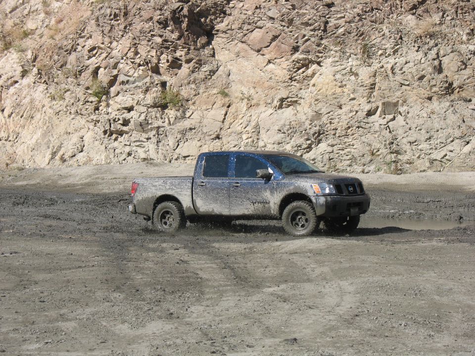 Nissan Titan pickup truck driving through mud with rocky hillside in background