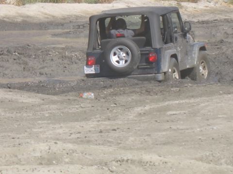 1987 Ford Bronco - A dark blue Jeep Wrangler is stuck in thick mud, with its rear end visible.