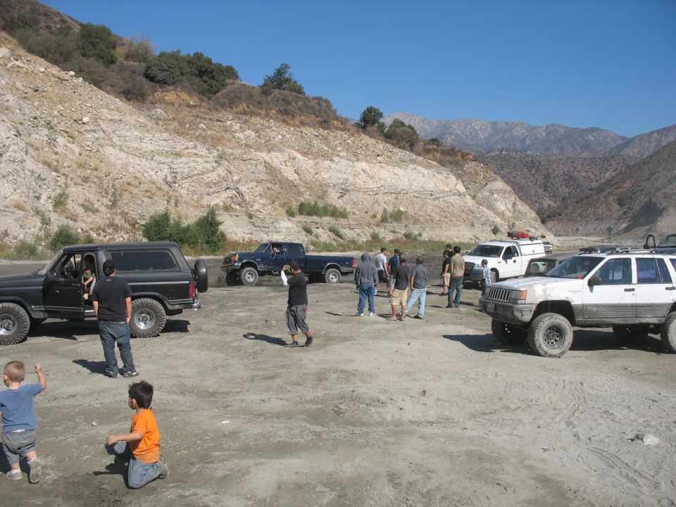 Several off-road vehicles parked in a dry riverbed with people and children present
