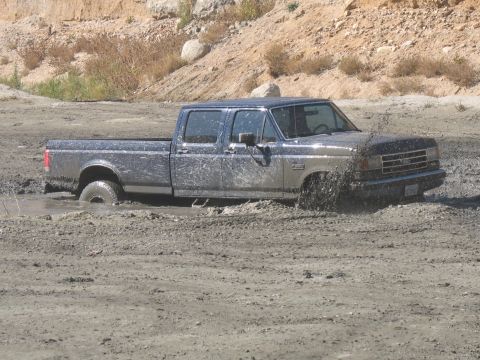1987 Ford Bronco - A 1987 Ford F-Series pickup truck is stuck in the mud, with water and dirt splashing around its tires.