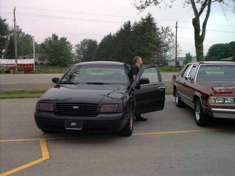 2000 Ford Crown Victoria - A black 2000 Ford Crown Victoria is parked with its driver's door ajar, alongside another sedan.
