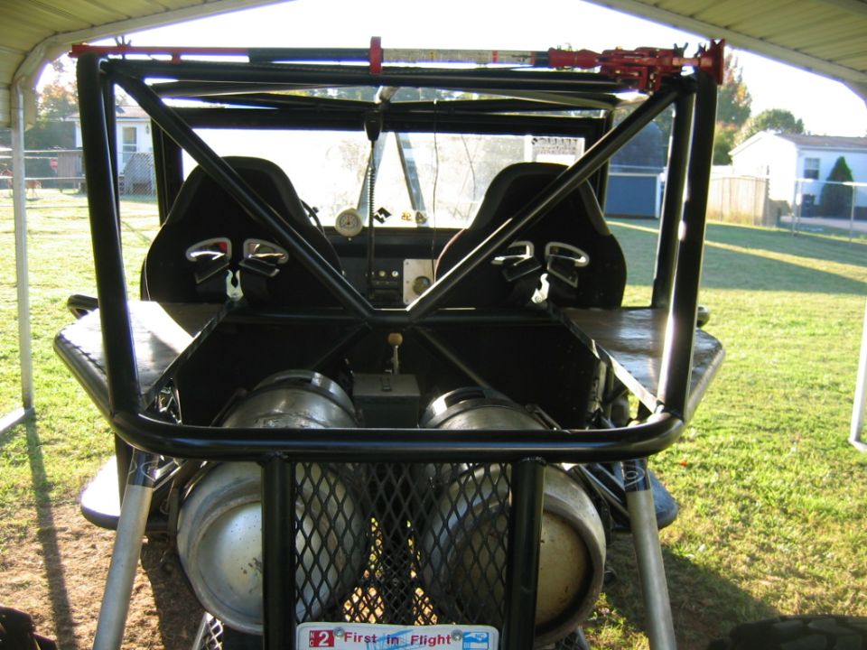 Custom off-road vehicle interior with two bucket seats, roll cage, two large tanks, and a license plate reading "First in Flight"