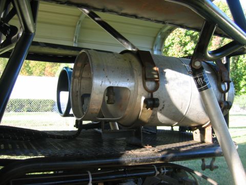 1992 Ford Mustang - Close-up of a propane tank mounted on a metal structure, with trees and a fence in the background.