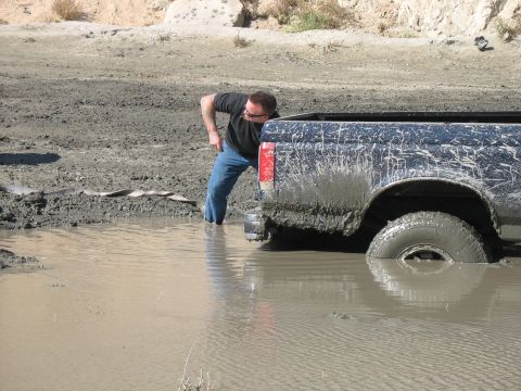 1987 Ford Bronco - A person inspects a mud-covered 1987 Ford Bronco that is stuck in a muddy puddle.