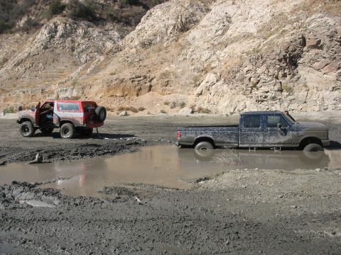 1987 Ford Bronco - Two off-road vehicles are stuck in deep mud in a dry riverbed.