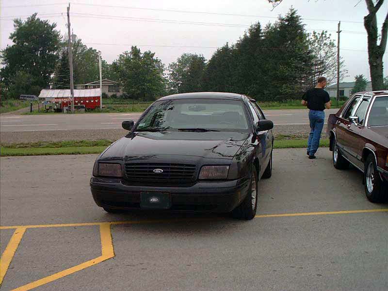 Black Ford Crown Victoria parked head-on in a lot with yellow-striped pavement