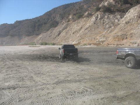 1987 Ford Bronco - Two pickup trucks navigate a challenging terrain with a mountain backdrop.