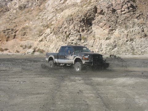 1987 Ford Bronco - This truck is navigating a muddy terrain with a rocky hillside visible behind it.