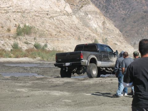 1987 Ford Bronco - A black Ford F-250 truck navigates a muddy terrain with onlookers present.