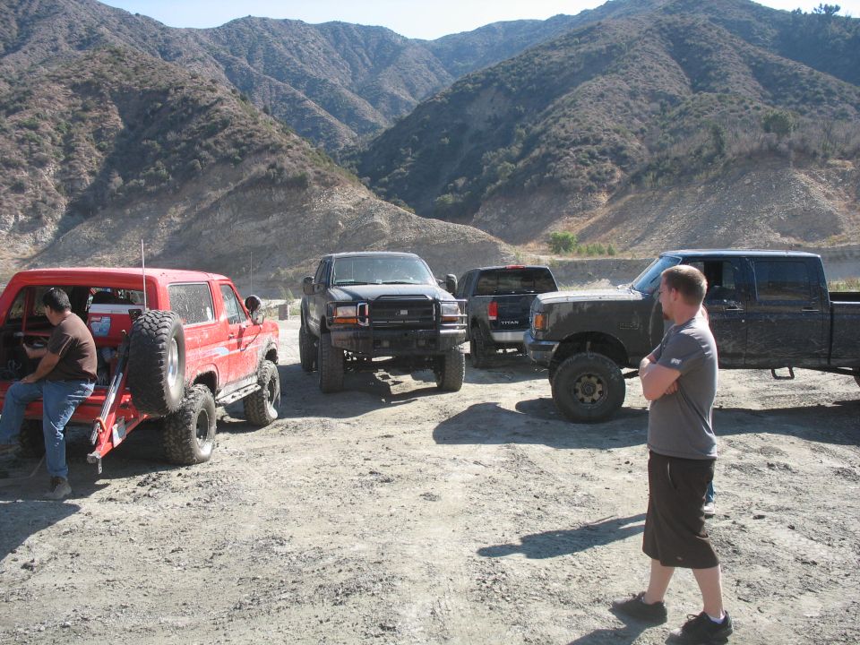 Red SUV with spare tire, black pickup, dark gray pickup, and man in a mountainous area