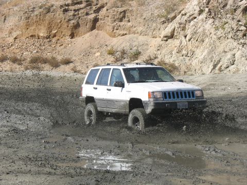 1987 Ford Bronco - White Jeep Grand Cherokee driving through a muddy terrain.
