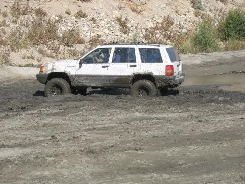 1987 Ford Bronco - A white Jeep Grand Cherokee is stuck in thick mud, with its front wheels submerged.