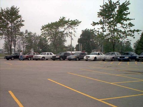 2000 Ford Crown Victoria - A row of sedans are parked in an outdoor lot under an overcast sky.