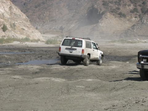 1987 Ford Bronco - White SUV navigates a challenging dirt road in a dry, mountainous area. Another vehicle is present.