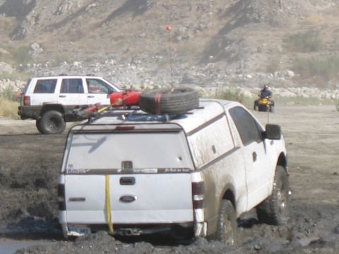 1987 Ford Bronco - Two off-road vehicles are stuck in the mud on a dry, rocky terrain.