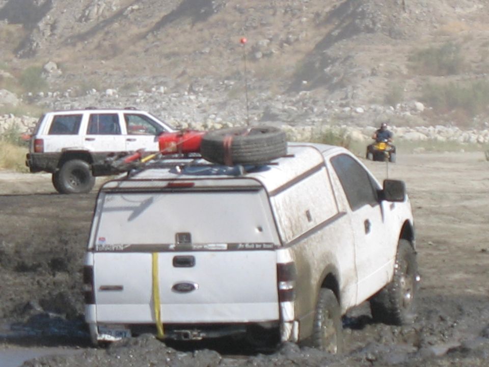 White pickup truck stuck in mud with spare tire on roof, white SUV behind it