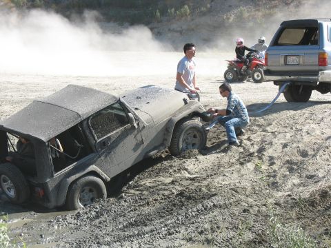 1987 Ford Bronco - A Jeep Wrangler is stuck in the mud while other vehicles and people are present at the scene.