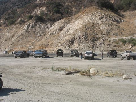 1987 Ford Bronco - A group of off-road vehicles are gathered in a dry, rocky terrain with a steep hillside in the background.