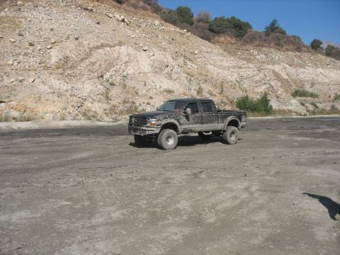 1987 Ford Bronco - A black Ford F-250 Super Duty truck is parked on a dirt road with a rocky hillside in the background.