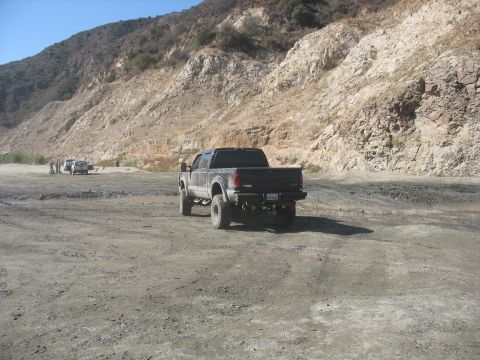 1987 Ford Bronco - A black Ford F-250 Super Duty pickup truck is parked in a dry, rocky landscape with other vehicles in the distance.