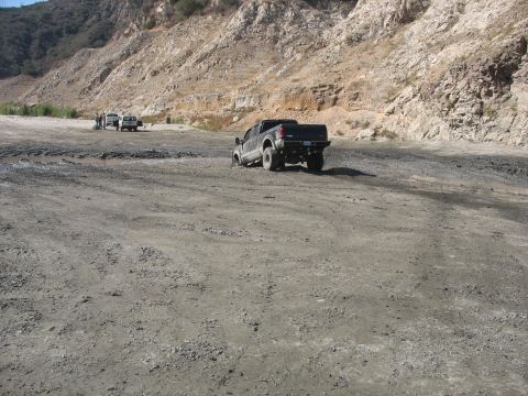 1987 Ford Bronco - Several vehicles navigate a dusty, off-road terrain with a mountainous backdrop.
