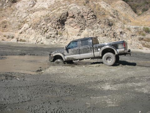 1987 Ford Bronco - Pickup truck is stuck in a muddy area with a rocky hillside in the background.