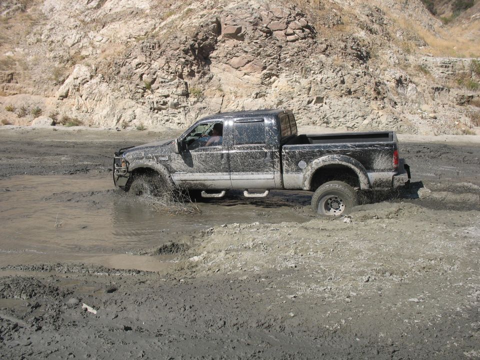 Black pickup truck with mud splashing as it drives through a muddy area