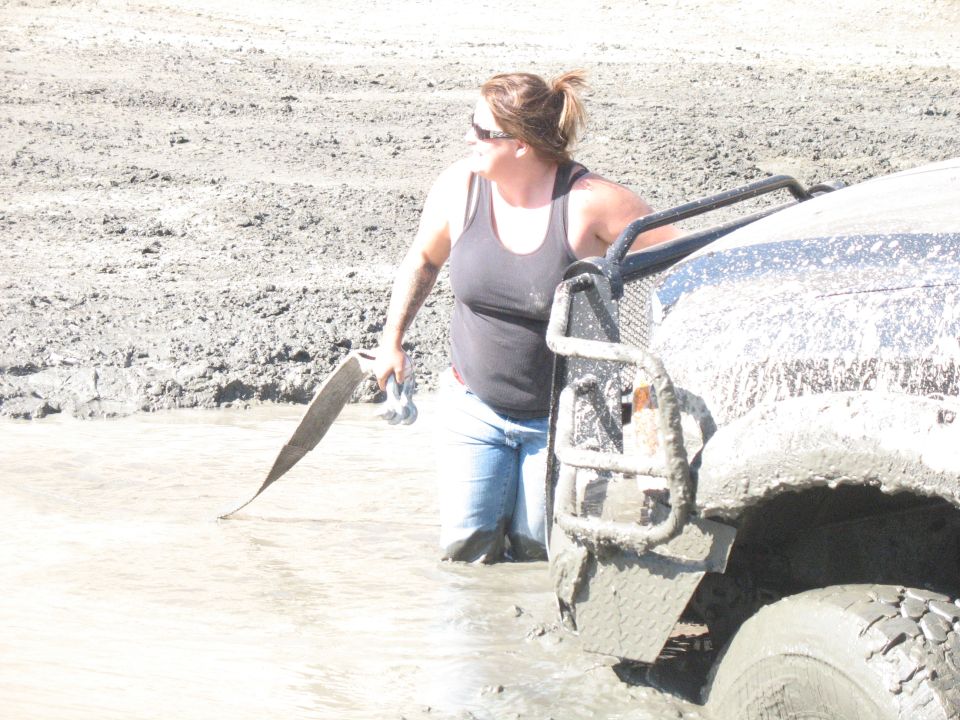 Mud-covered vehicle front corner with woman in water holding tow strap