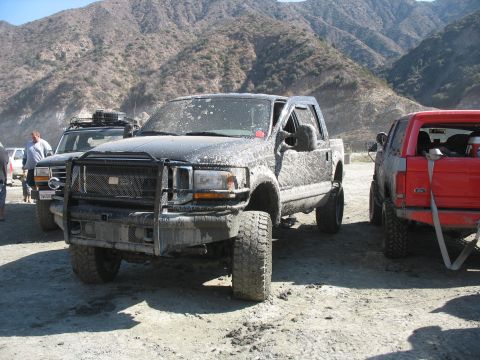1987 Ford Bronco - A muddy black Ford F-250 truck is parked outdoors with other vehicles and mountains in the background.