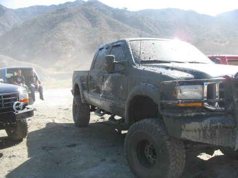 1987 Ford Bronco - A heavily mud-splattered pickup truck sits in a dusty, outdoor environment with mountains in the background.