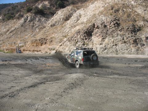 1987 Ford Bronco - A 1987 Ford Bronco navigates a muddy terrain, sending dirt flying.