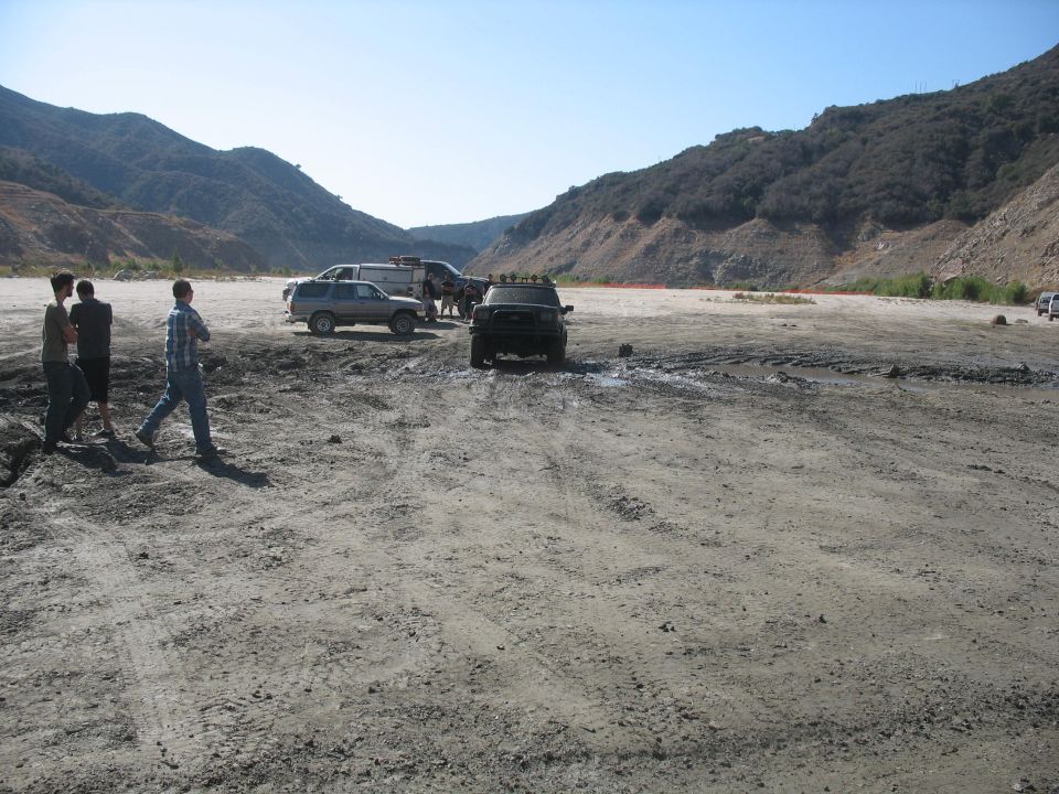 Black SUV with roof lights parked in muddy terrain, with other vehicles and people nearby