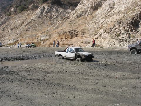 1987 Ford Bronco - A white pickup truck is stuck in a muddy area, with another vehicle visible in the background.