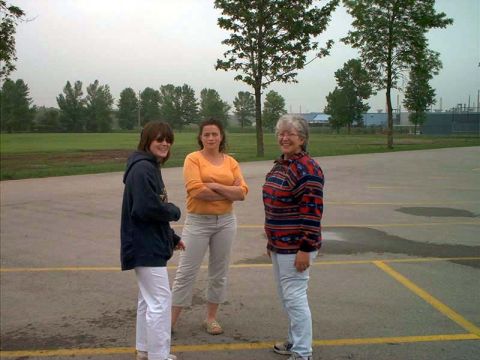 2000 Ford Crown Victoria - Three women stand together in an empty yellow-striped parking lot on an overcast day, one in a navy hoodie, one in an orange sweater and on…