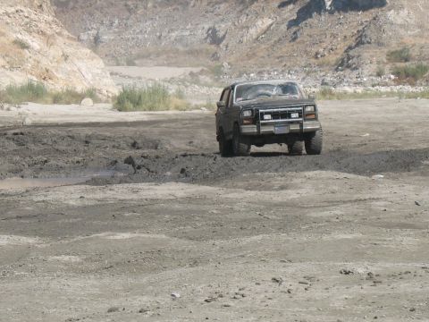 1987 Ford Bronco - A dark SUV navigates a muddy terrain in a rocky, arid landscape.