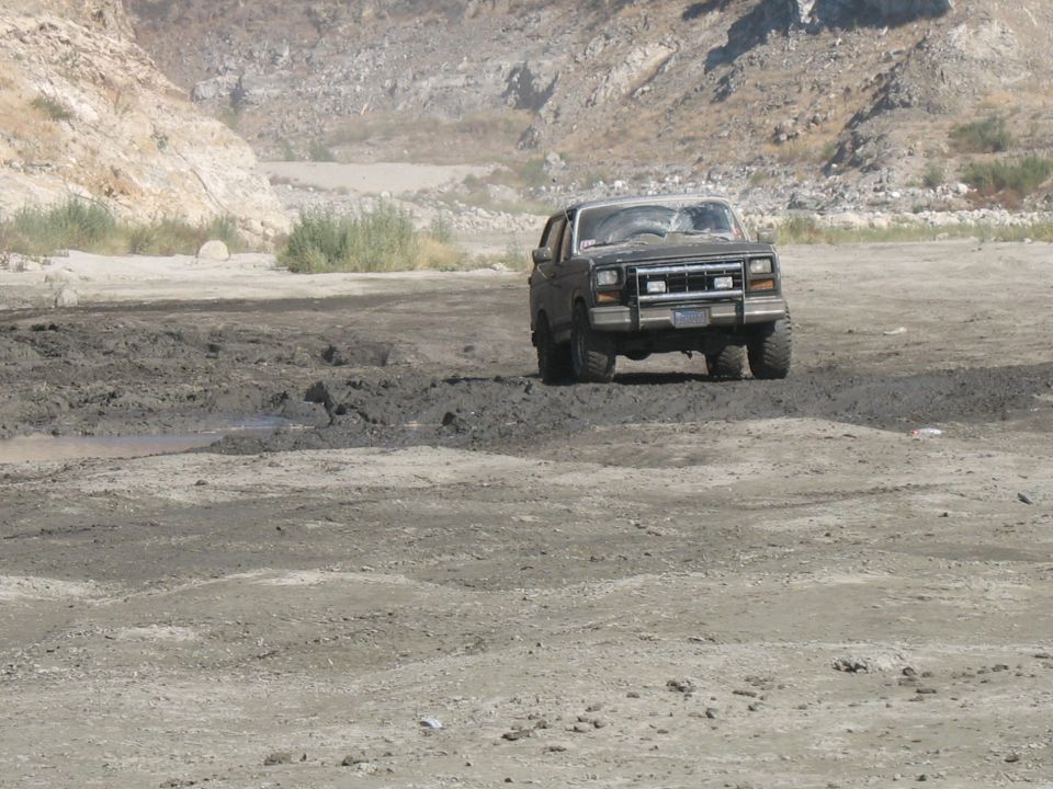 Dark SUV driving through mud, front grille and headlights visible