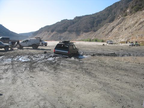 1987 Ford Bronco - A 1987 Ford Bronco is stuck in the mud while other vehicles and ATVs are nearby in a dry, hilly landscape.