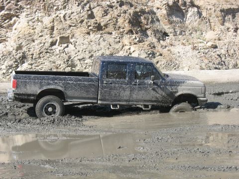 1987 Ford Bronco - This four-door pickup truck is deeply stuck in thick mud, with its front tires submerged.