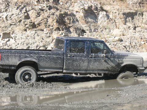 1987 Ford Bronco - A dark blue 1992 Ford F-Series truck is stuck in deep mud, with its front wheel submerged.
