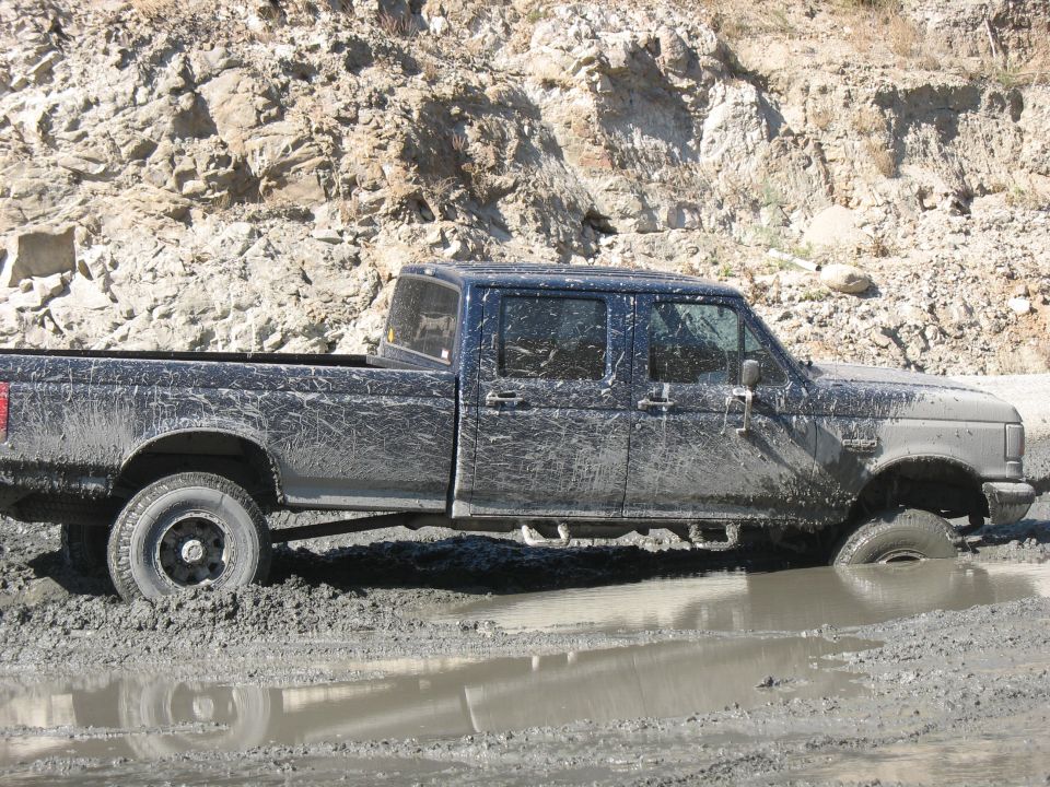 Mud-covered dark blue 1992 Ford F-Series truck stuck in mud, side view