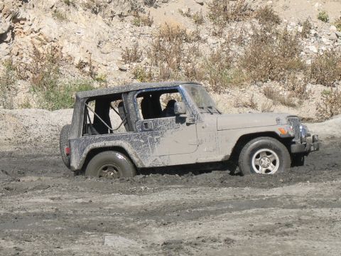 1987 Ford Bronco - A Jeep Wrangler is stuck in thick mud, with its tires submerged and mud splattered across its body.