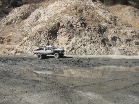 1987 Ford Bronco - Pickup truck navigates a challenging muddy terrain with large puddles and tire tracks.