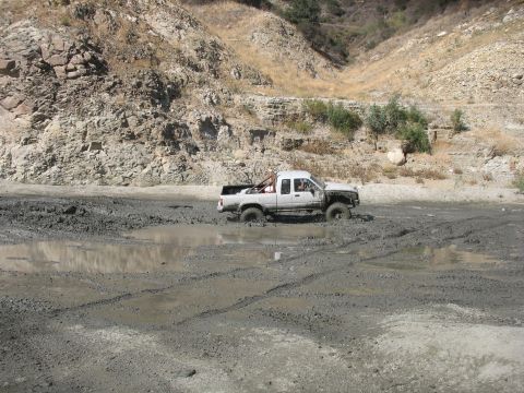 1987 Ford Bronco - A white pickup truck navigates through a muddy terrain with deep tire tracks visible.