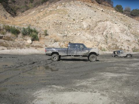 1987 Ford Bronco - Two off-road vehicles are stuck in thick mud on a dry, rocky hillside.