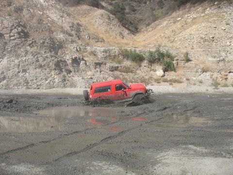 1987 Ford Bronco - A red 1987 Ford Bronco navigates a muddy off-road course, kicking up dirt as it gets stuck.