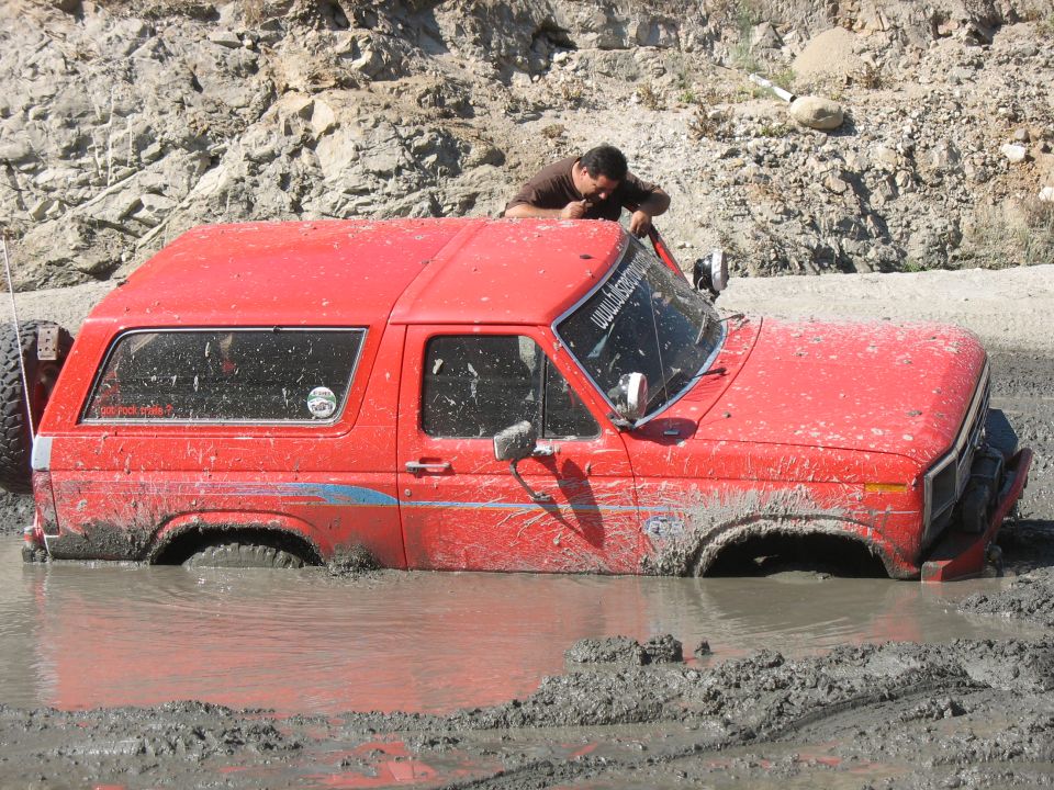 Red SUV stuck in mud, front 3/4 view. Mud covers the vehicle up to the doors