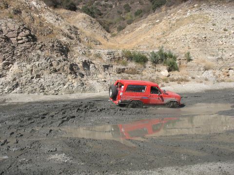 1987 Ford Bronco - A red 1987 Ford Bronco is stuck in deep mud, with its tires submerged.