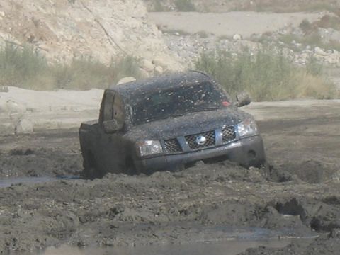 1987 Ford Bronco - A Nissan Titan truck is stuck in a muddy area, with its front end submerged in the mire.